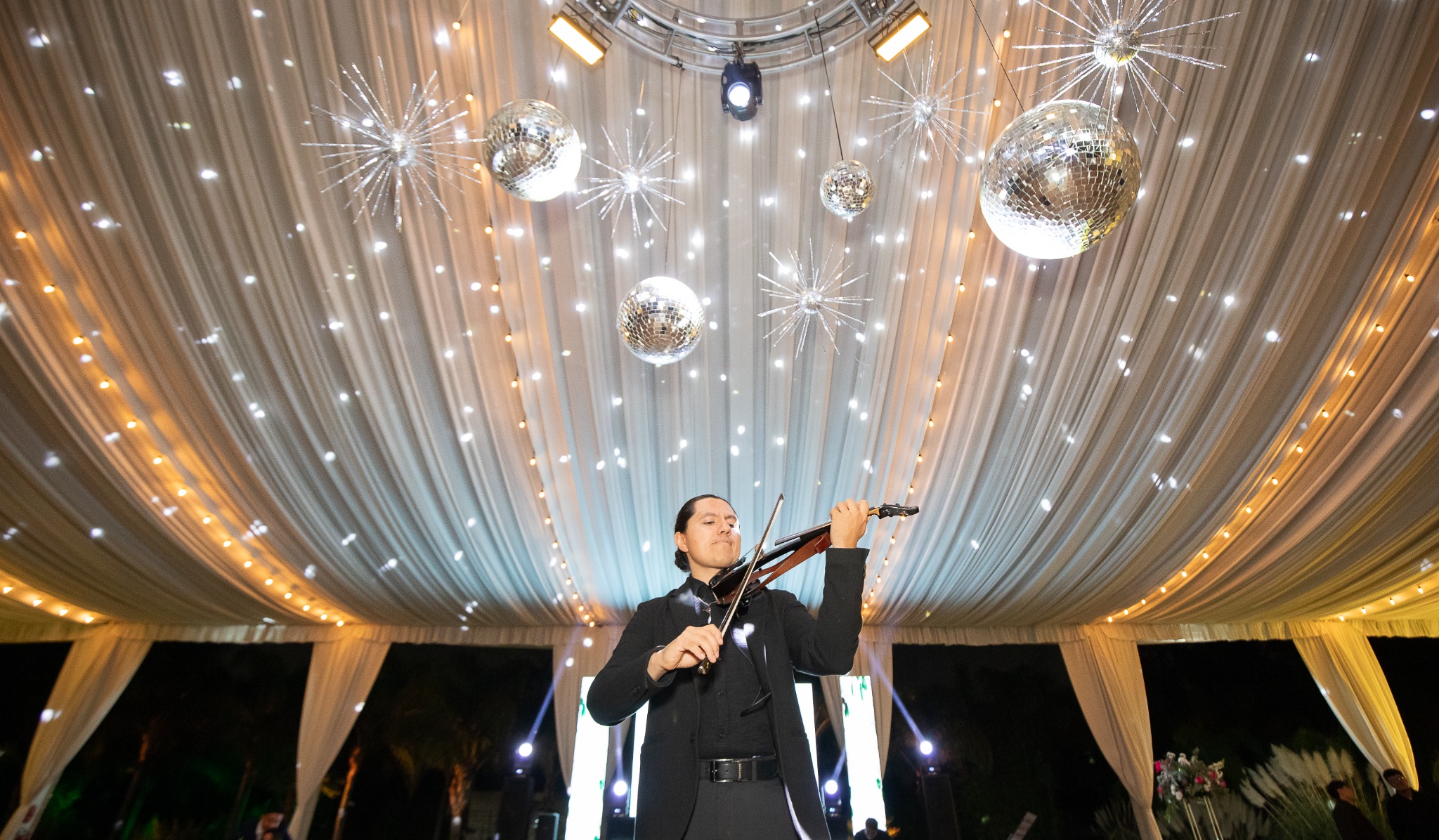 Miguel Fajardo interpretando el violín en una celebración bajo luces cálidas y esferas de cristal