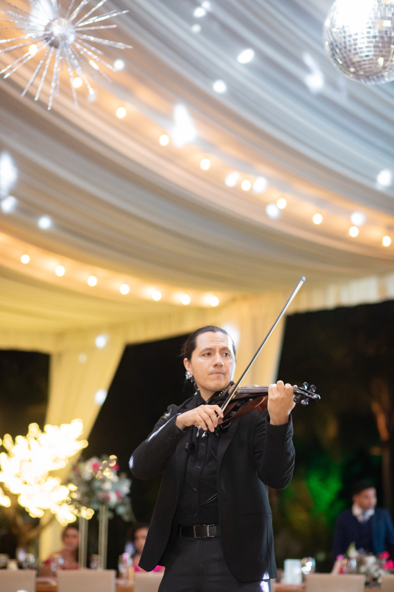 Miguel interpretando el violín entre luces y esferas brillantes durante un evento